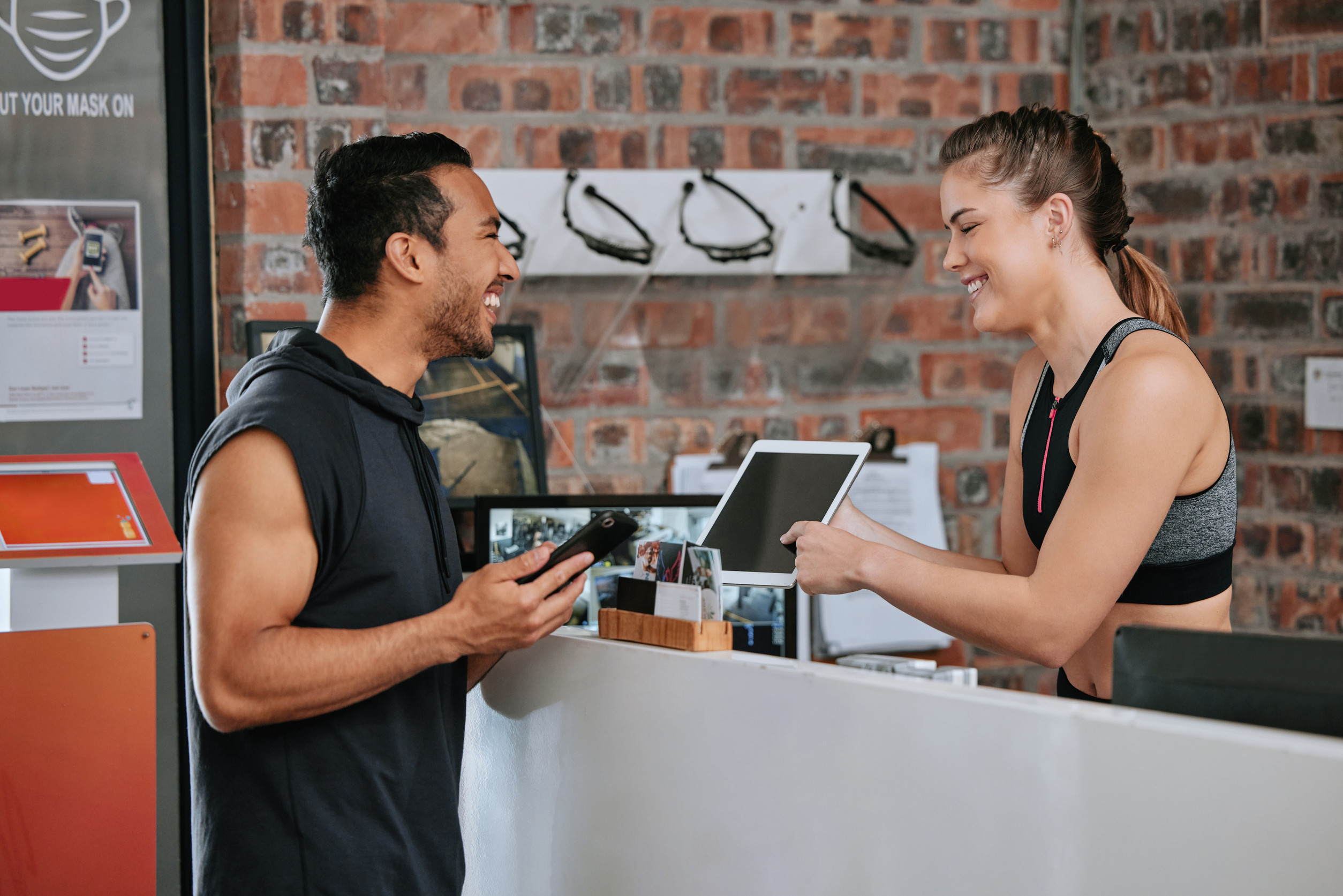 Asian man joining gym on digital tablet as member with caucasian trainer. Young coach helping, pointing and showing plan on technology. Two active fit people standing together in healthy fitness club.
