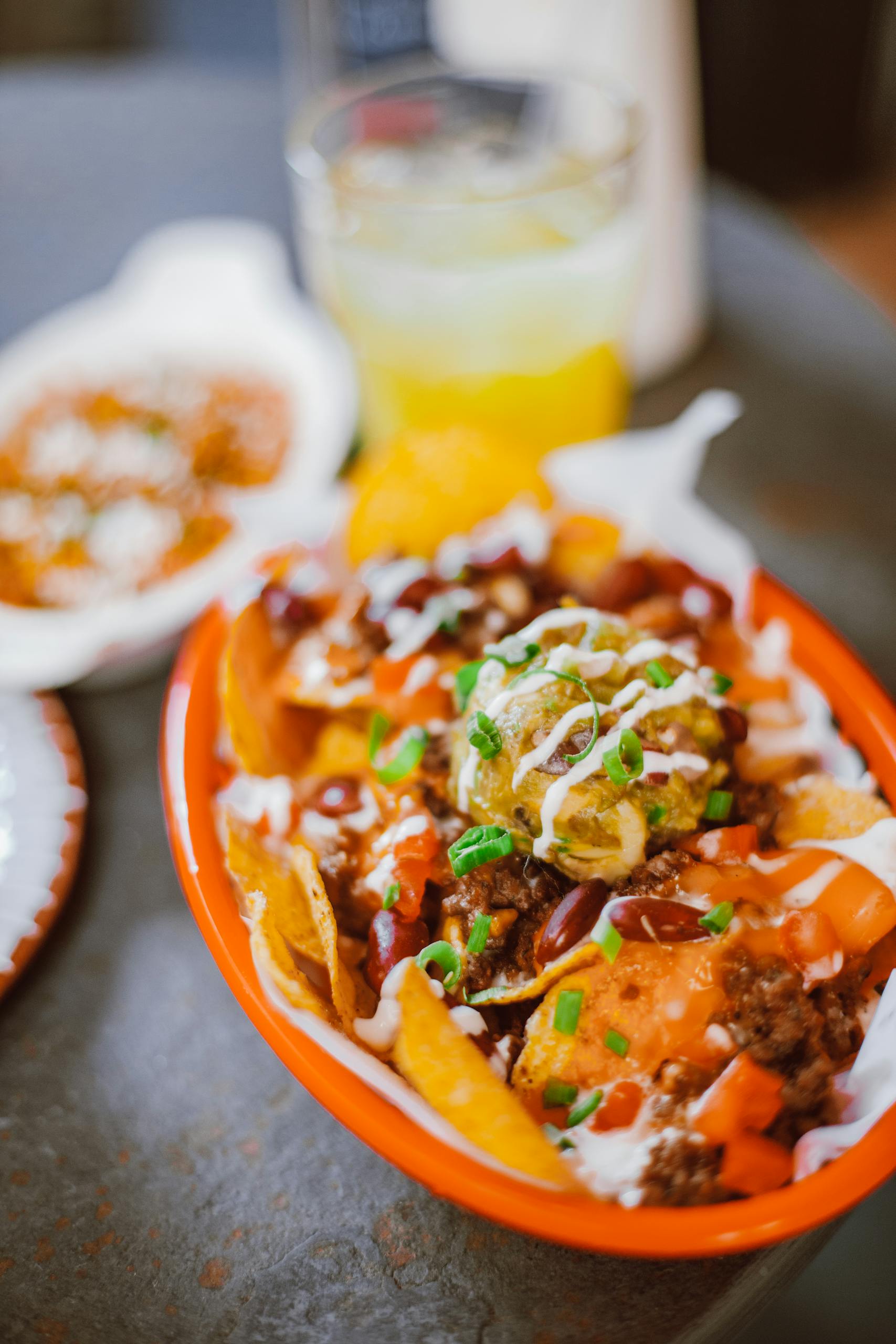 Close-up of loaded nachos with cheese, guacamole, salsa, and chives in a red bowl.