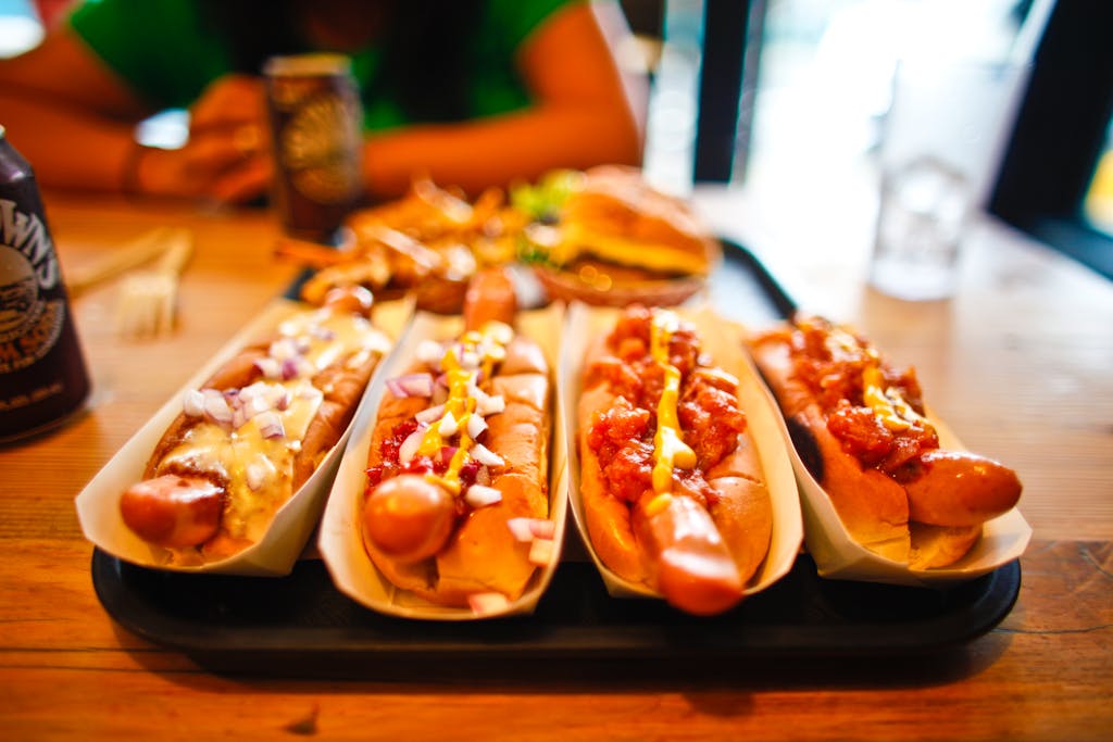 If You Eat These 8 Foods Daily, Your Health Could Be at Risk 4 Close-up of various hotdogs with toppings on a wooden table, ideal for fast food themes.