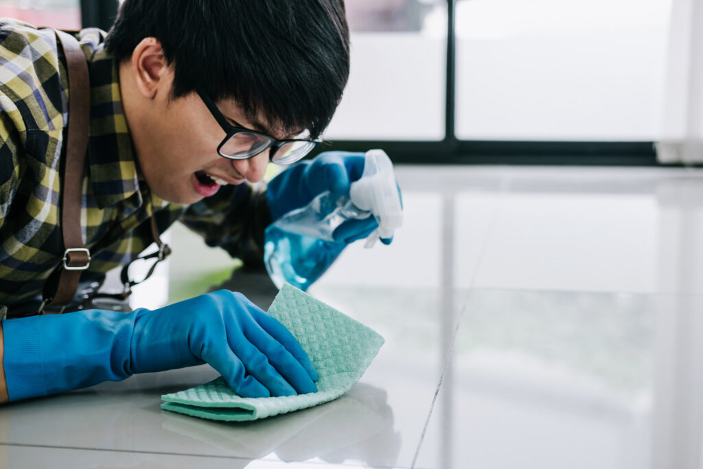 usband housekeeping and cleaning concept, Happy young man in blue rubber gloves wiping dust using a spray and a duster while cleaning on floor at home.