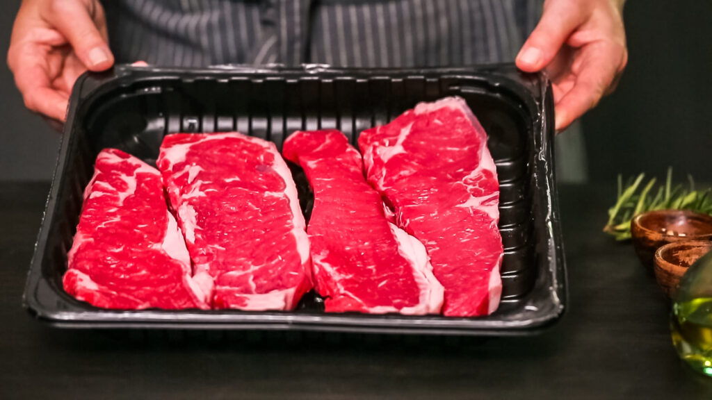 Raw New York strip steaks on a wood cutting board.