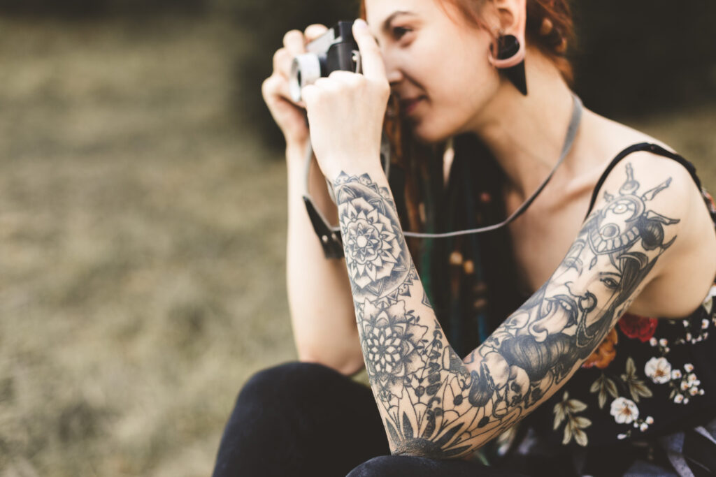 young girl with tattoos and dreadlocks photographs vintage camera in the park