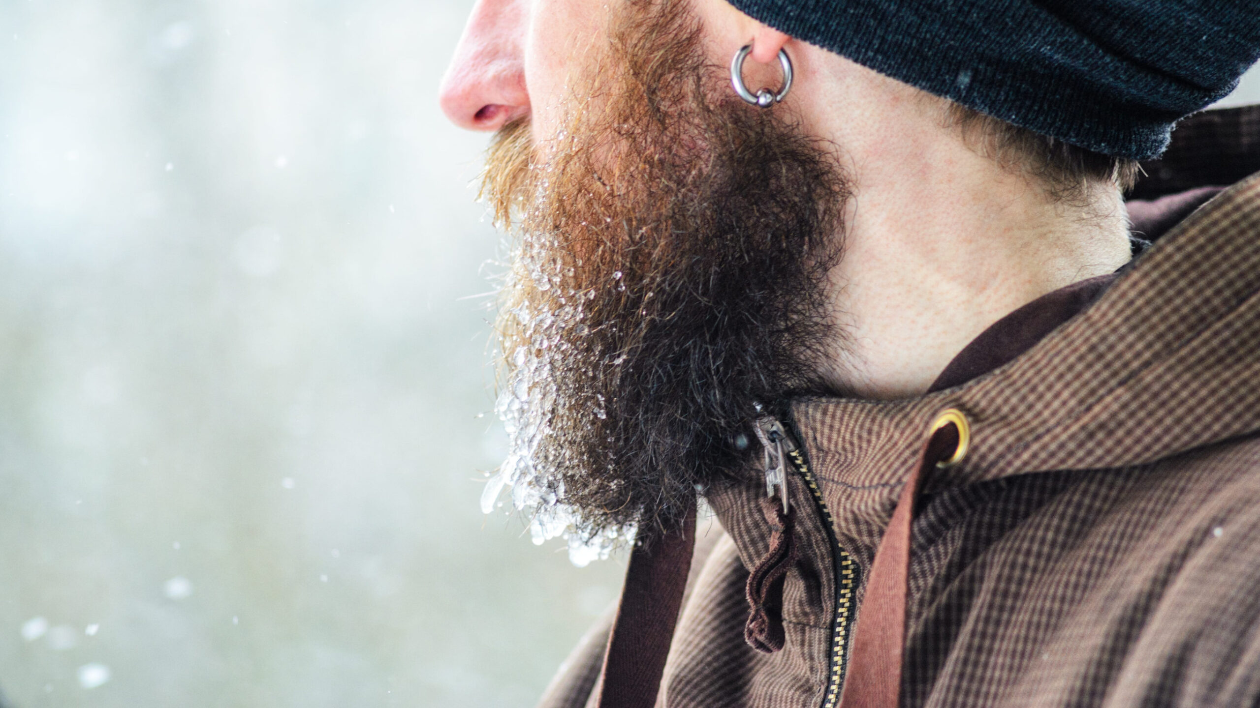 Beard covered with icicles and frozen droplets. Young man winter portrait in profile.