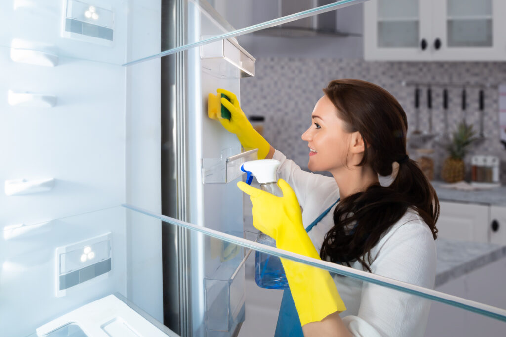 Close-up Of A Happy Young Woman Cleaning Refrigerator With Sponge