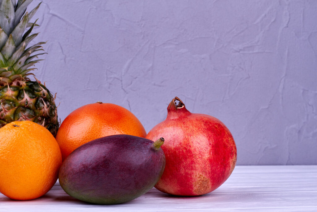 Assortment of colorful tropical fruits. Fresh mango, pomegranate, grapefruit, orange and pineapple on wooden background. Delicious summer ingredients.