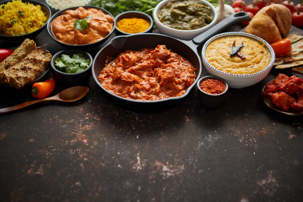 Assortment of various kinds of Indian cousine on dark rusty table. Chicken Tikka Masala, Butter, Nilgiri, Daal Tarka. Served with fried rice, naan bread and spices. Flat lay with copy space.