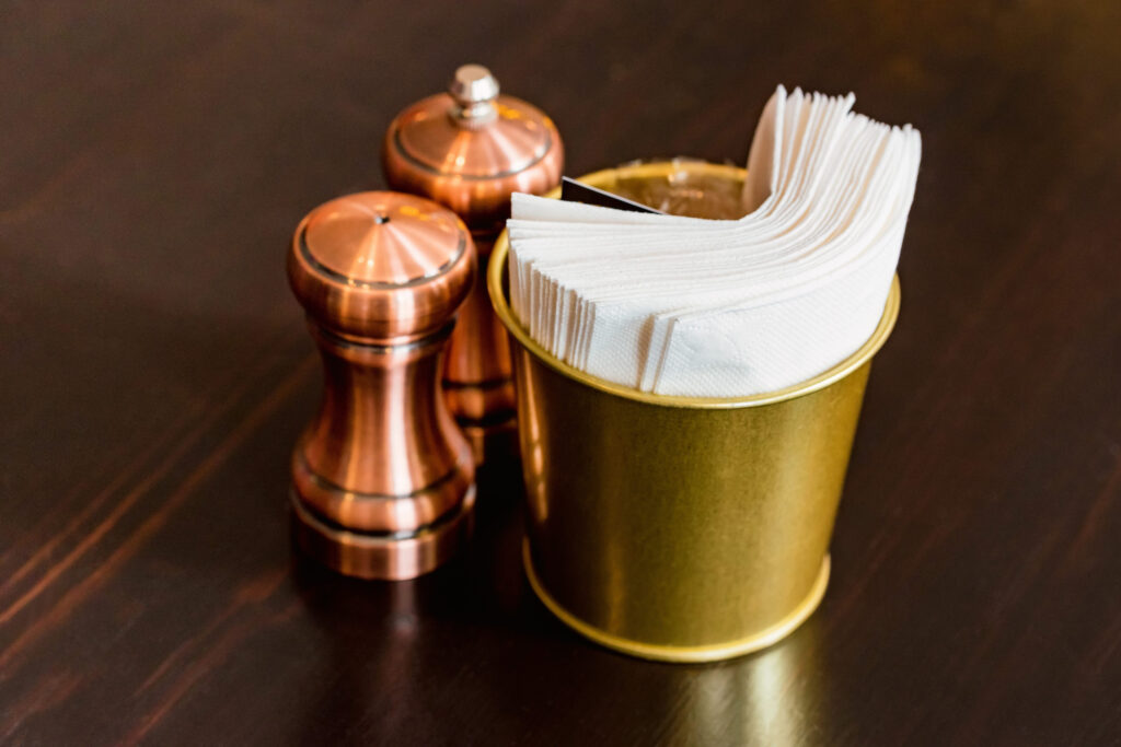 Salt in brown chrome casters and bucket with napkins in restaurant