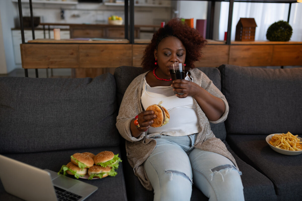 Home atmosphere. Concentrated brunette drinking cola and eating hamburger