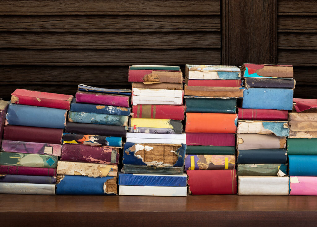 Heap up of old and damaged book on wooden table with wooden wall background