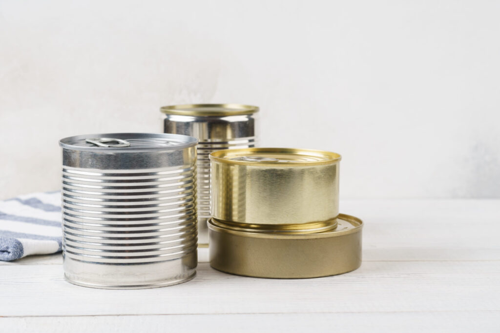 Various closed tin cans with food preserves on a light gray background. Canned food concept. Food donations. Copy space.