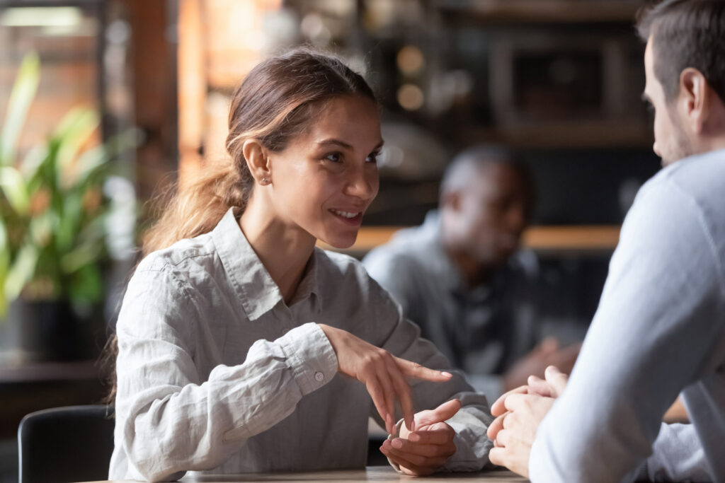 Attractive smiling mixed race woman chatting with man in coffeehouse, sitting together at table, having pleasant conversation, couple talking, flirting on date, having fun together at meeting