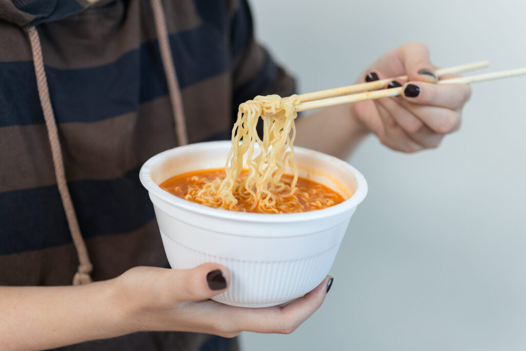 Bowl of instant noodles ramen in hands with chopsticks, close up