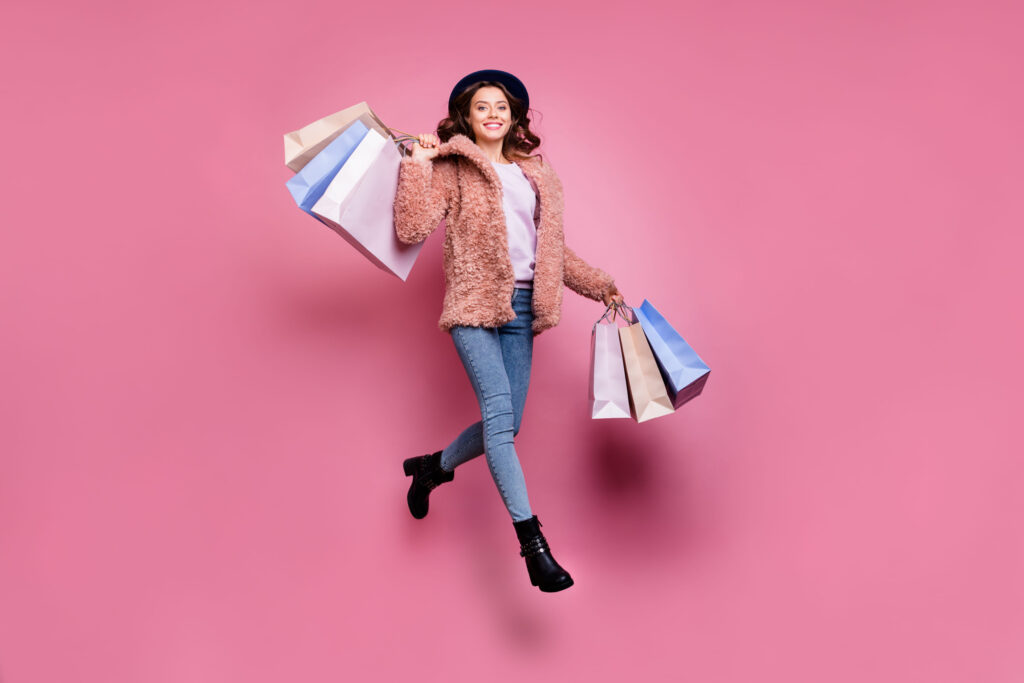 Full length photo of beautiful model millennial lady jumping high enjoy sales carry many packs store wear fluffy jacket retro blue hat jeans isolated pink background