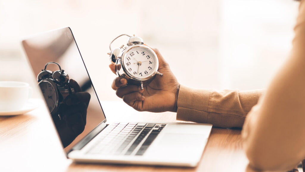 Most People Over 40 Who Lack These 9 Skills Are Struggling in Silence 1 Time Management Concept. Black businessman holding alarm clock, working on laptop. Panorama, copy space