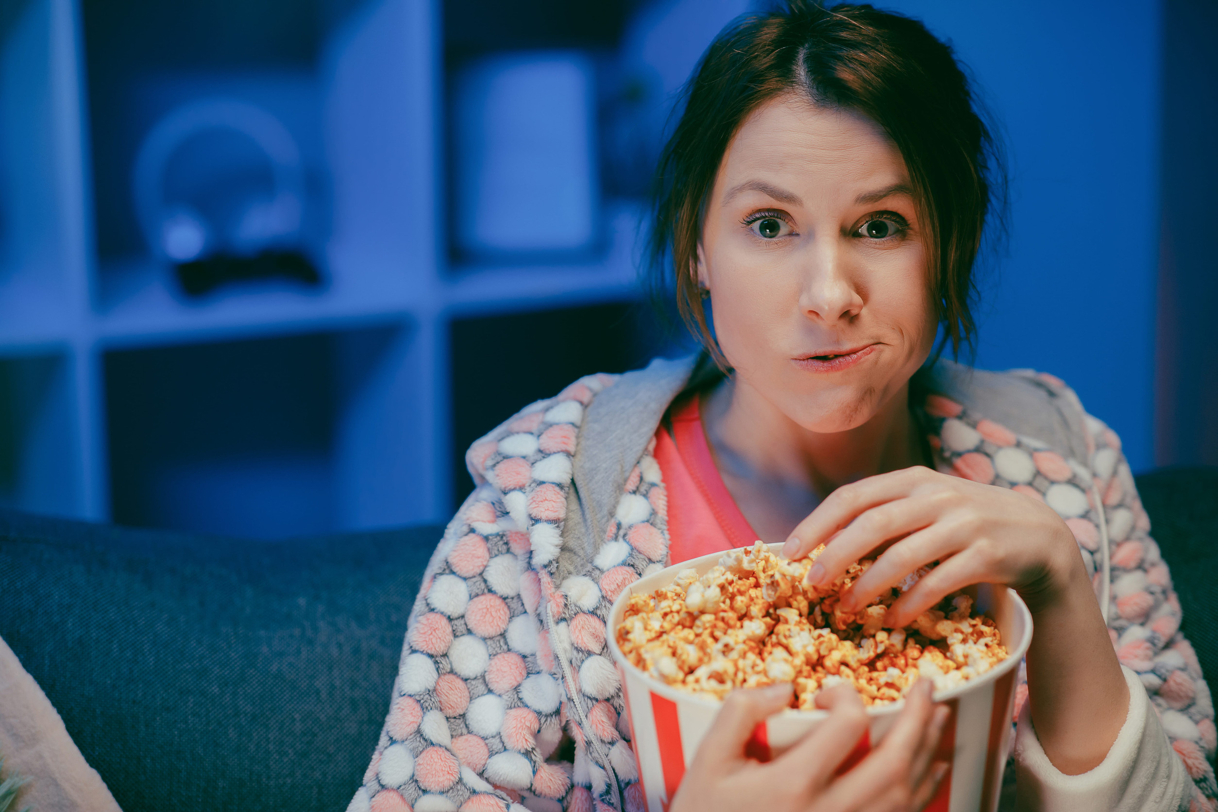Young lady is watching TV laughing and eating popcorn having fun at home alone enjoying modern television. Youth lifestyle and cheerful people concept