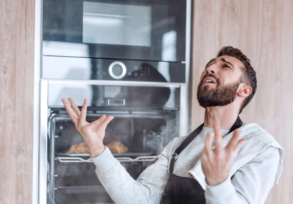 surprised man standing near the oven with burnt croissants.