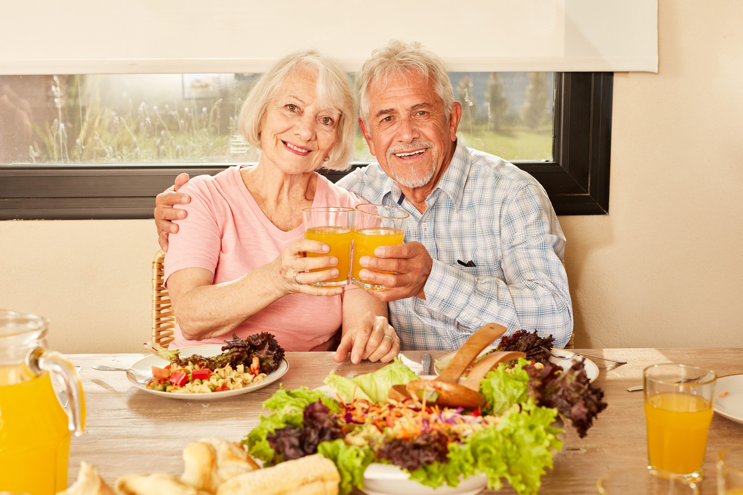 Couple of seniors toasting with orange juice at vegetarian lunch