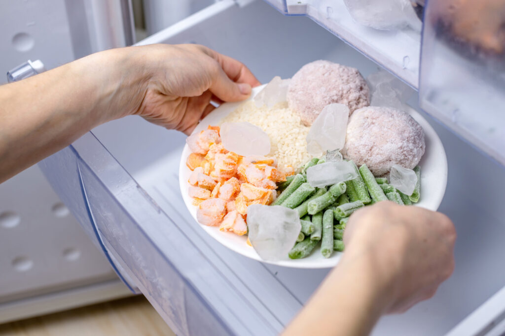 Women's hands are taking a plate of frozen food from the freezer of the fridge. Concept of storing ready made dinner and saving time.