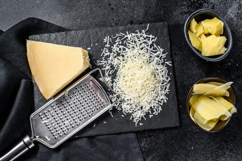 Italian hard Parmesan cheese slice, cut, grated. Black background. Top view.