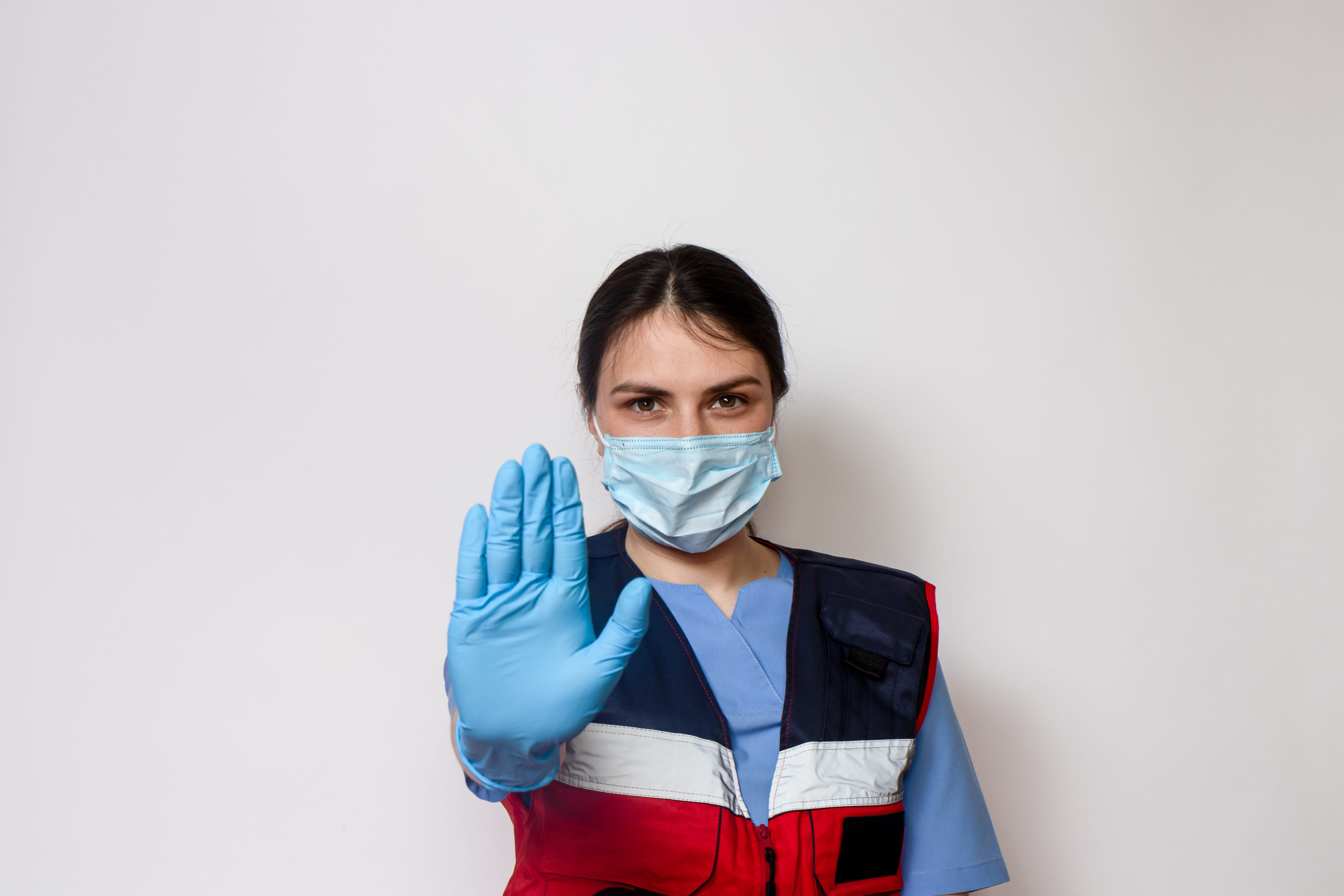 An ambulance doctor wearing a medical mask and gloves shows a stop sign.