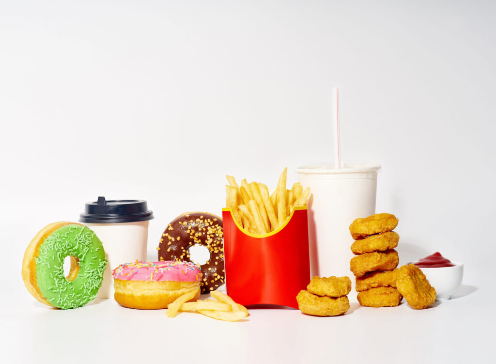 Junk food meal on white background. French fries, chicken nuggets, sweet glazed colorful donuts with drinks and sauce.