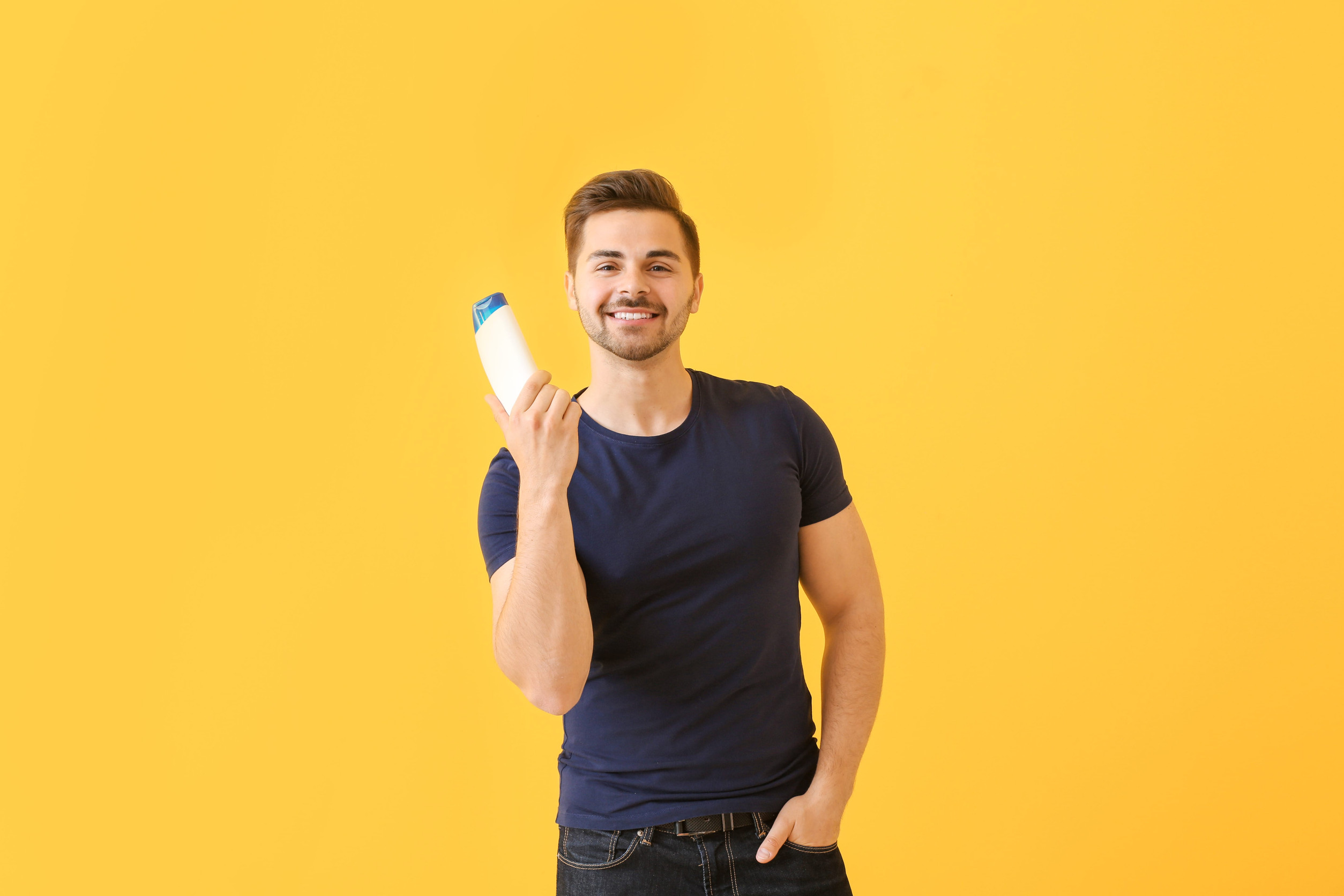Handsome man with bottle of shampoo on color background