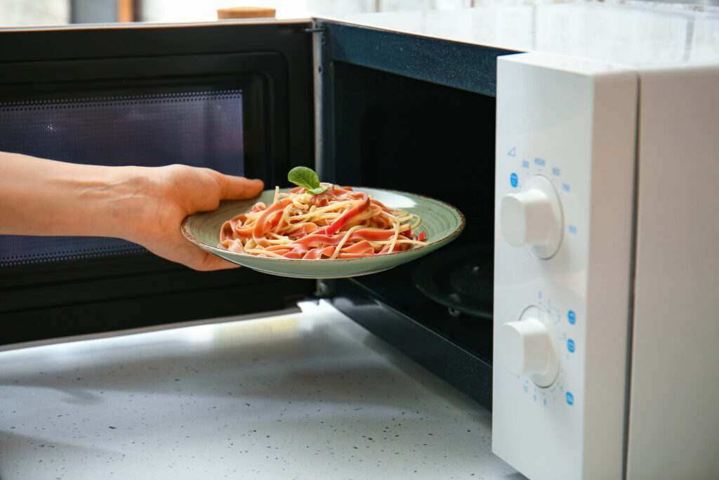 Woman putting plate with food in microwave oven