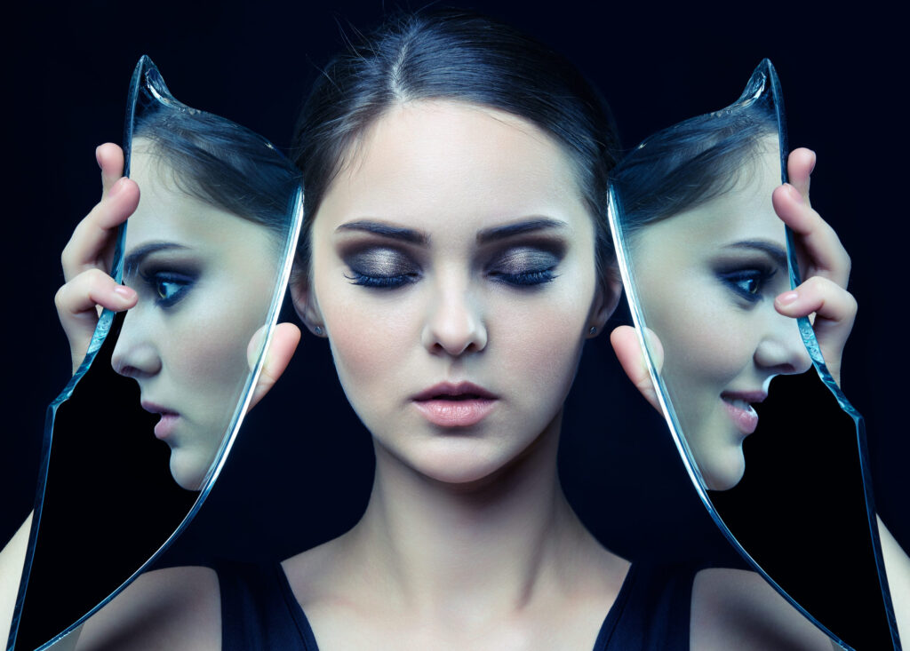 Girl with a shard of the mirror. Female with mirror shard in hand posing on gray background. Face reflection in mirror splinter. Eyes closed.