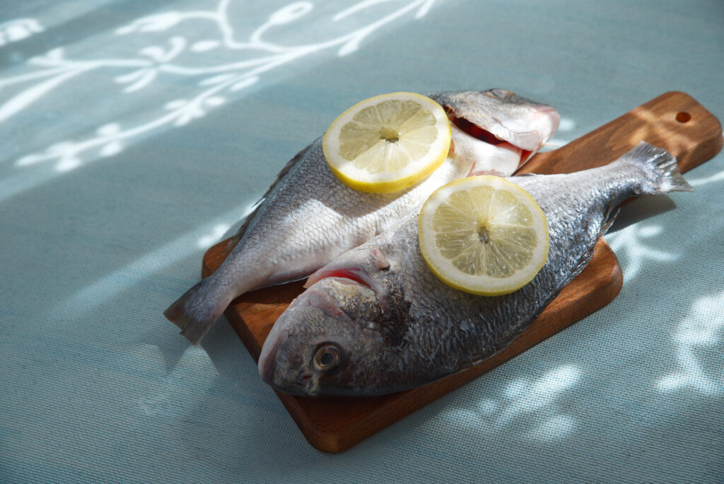 Fish with lemon slices on a wooden board and a light blue table in the background.
