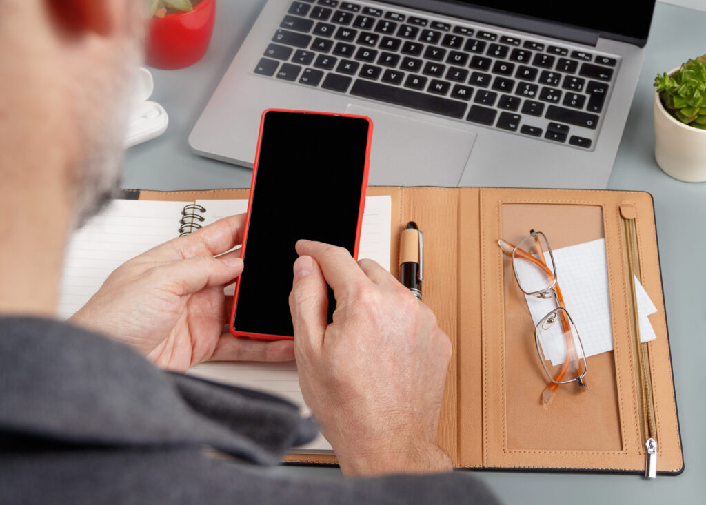 Man using cell phone and writing in agenda near laptop close up. Business concept