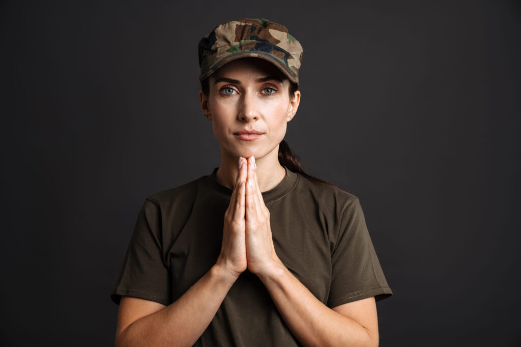 Calm beautiful soldier woman holding palms together isolated over black background
