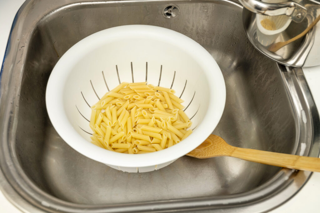 Draining macaroni to make an Italian pasta recipe with tomato and cheese