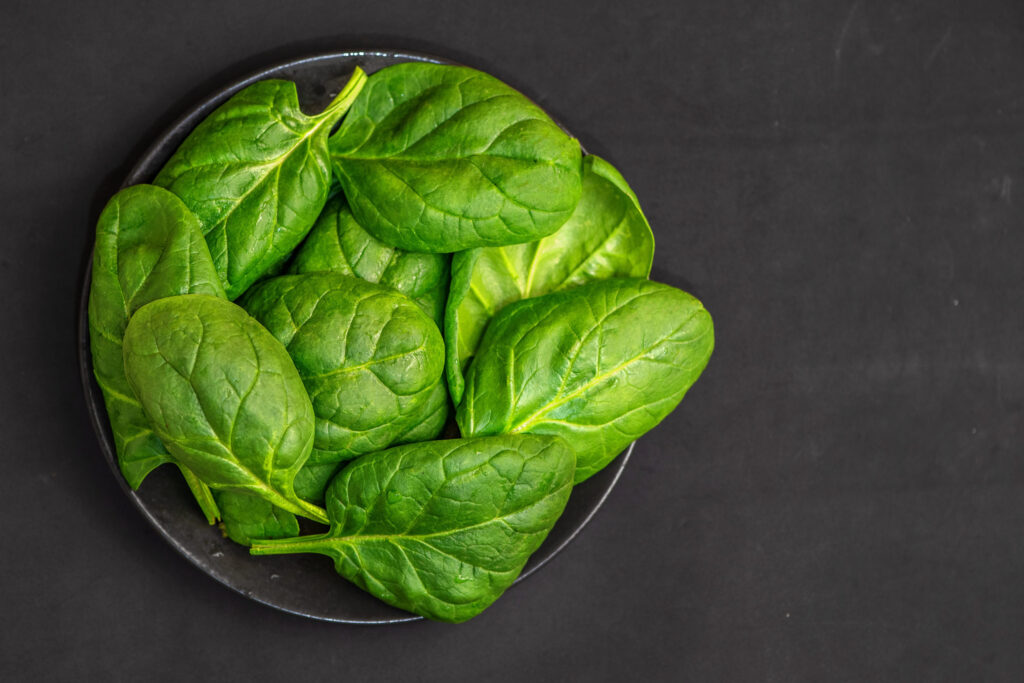 Fresh spinach leaves in bowl on dark background. Top view. With Copy Space.
