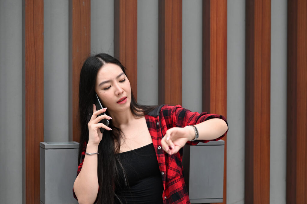 Young Asian woman talking on mobile phone while standing at outdoor shopping mall in the evening.