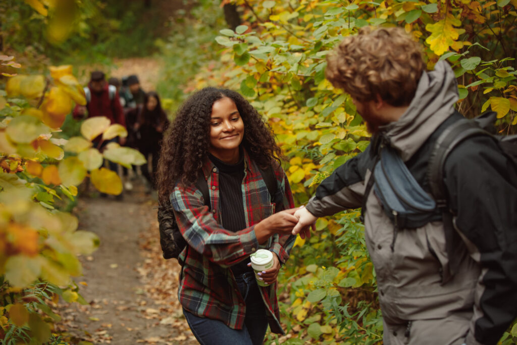 Cropped portrait of young beautiful couple spending time together with friends in the forest on warm autumn day. Hiking activity