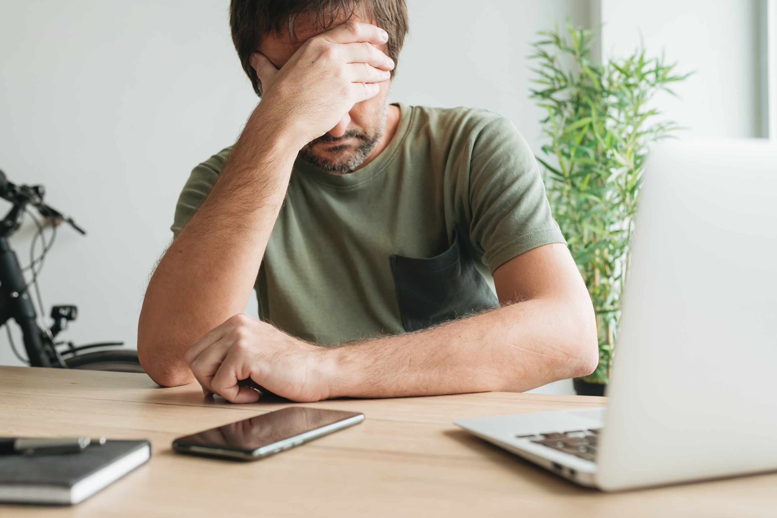 Disappointed telecommuter at home office desk covering face with his hand, selective focus