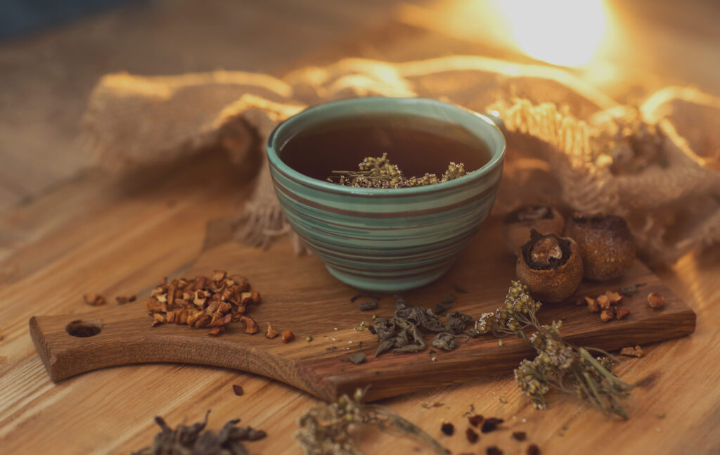 fragrant herbal tea in a cup, stands on a wooden surface next to dry herbs and berries. High quality photo
