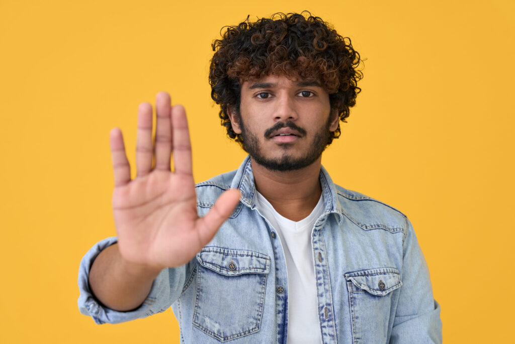 Young indian man showing stop hand gesture isolated on yellow background.