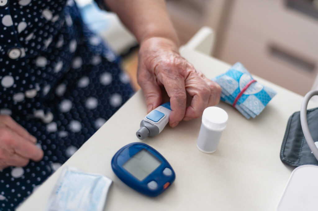 Senior Woman tests blood for glucose or sugar level for diabetes with glucometer, close up of hands, home kit for testing