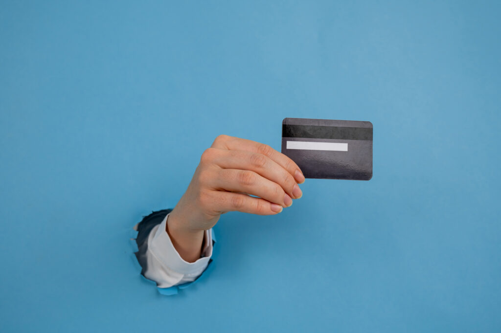 A woman's hand sticking out of a hole in a paper blue background holds a credit card