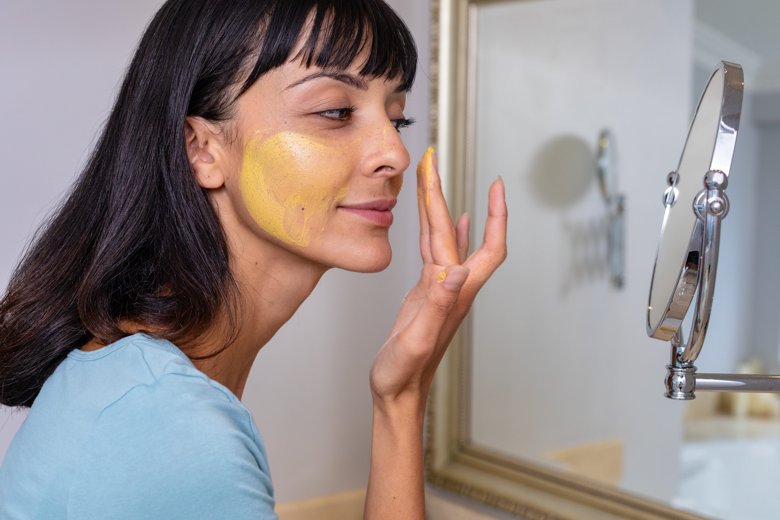 Caucasian young woman looking at mirror and applying facial mask in bathroom. unaltered, lifestyle, skin care, body care, beauty, beauty product.