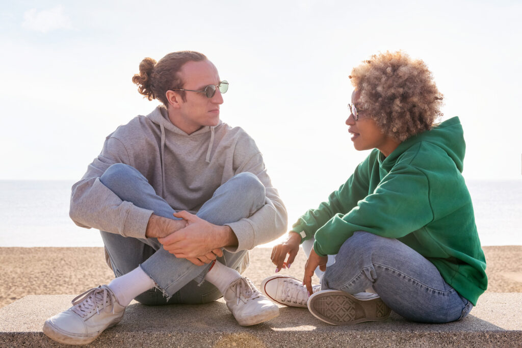 young couple chatting at sunset seated on a bench by the beach, concept of friendship and communication in a relationship