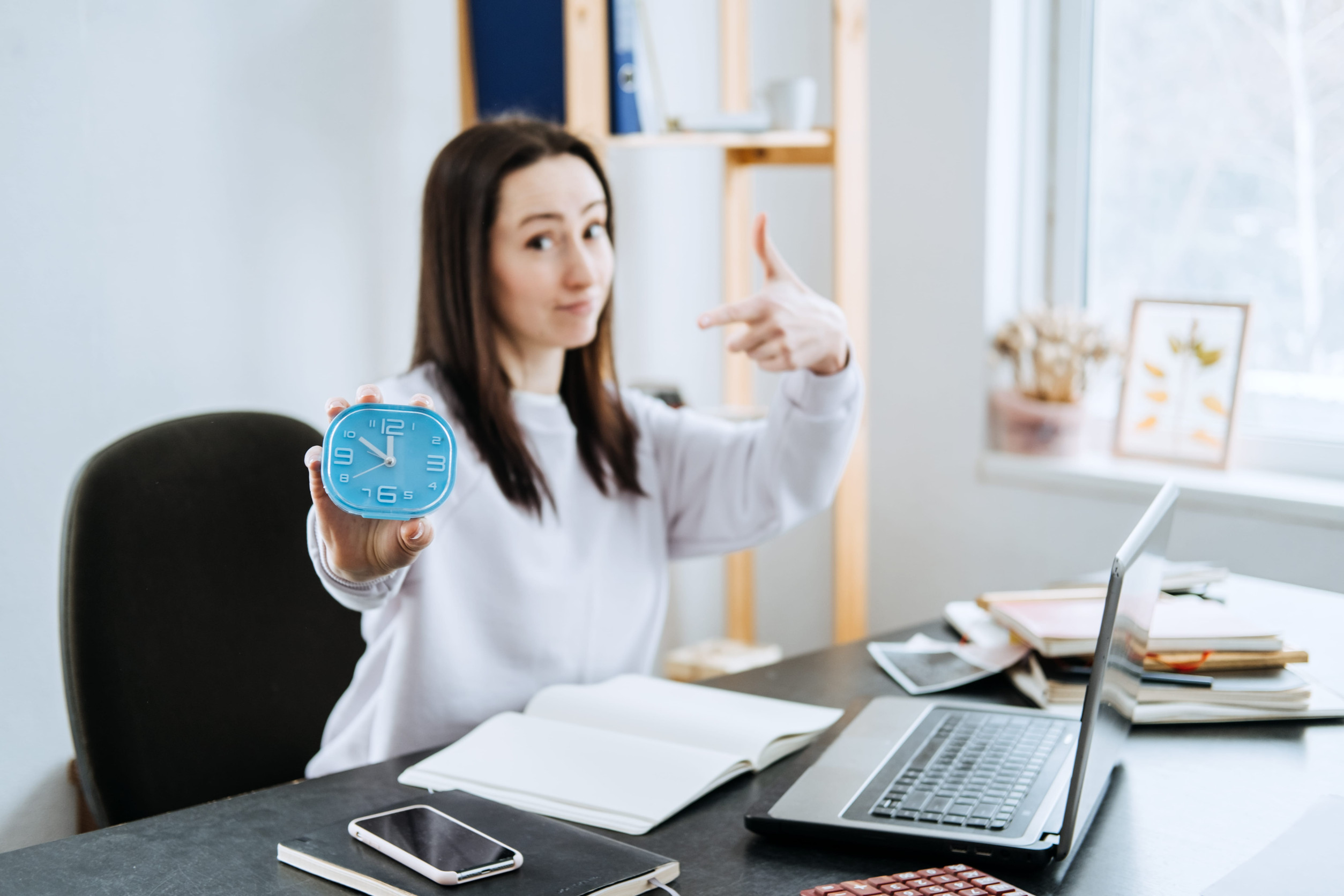 Accountant, businesswoman holding alarm clock in hands and points to the time.