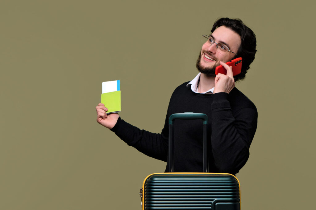 Bearded Man Traveler Tourist holds Fan Cash Dollars Banknotes and Flag USA. Guy in Casual Outfit and Red Eyewear Travels on Vacation Trip with Suitcase. Airline Passenger Transportation. Journey