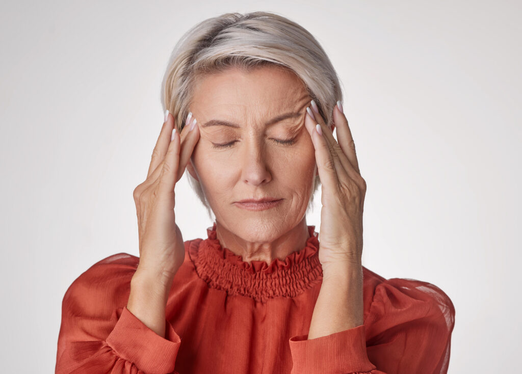 One mature woman suffering with a headache and looking stressed while posing against a grey copyspace background. Ageing woman experiencing anxiety and fear in a studio.