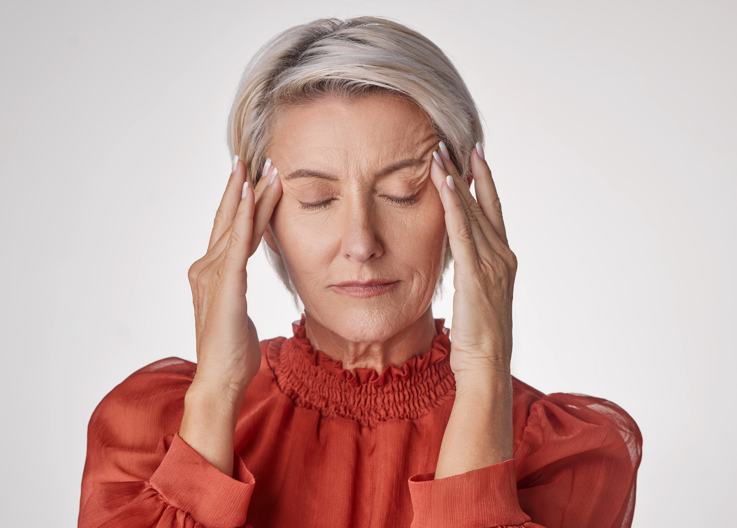One mature woman suffering with a headache and looking stressed while posing against a grey copyspace background. Ageing woman experiencing anxiety and fear in a studio.