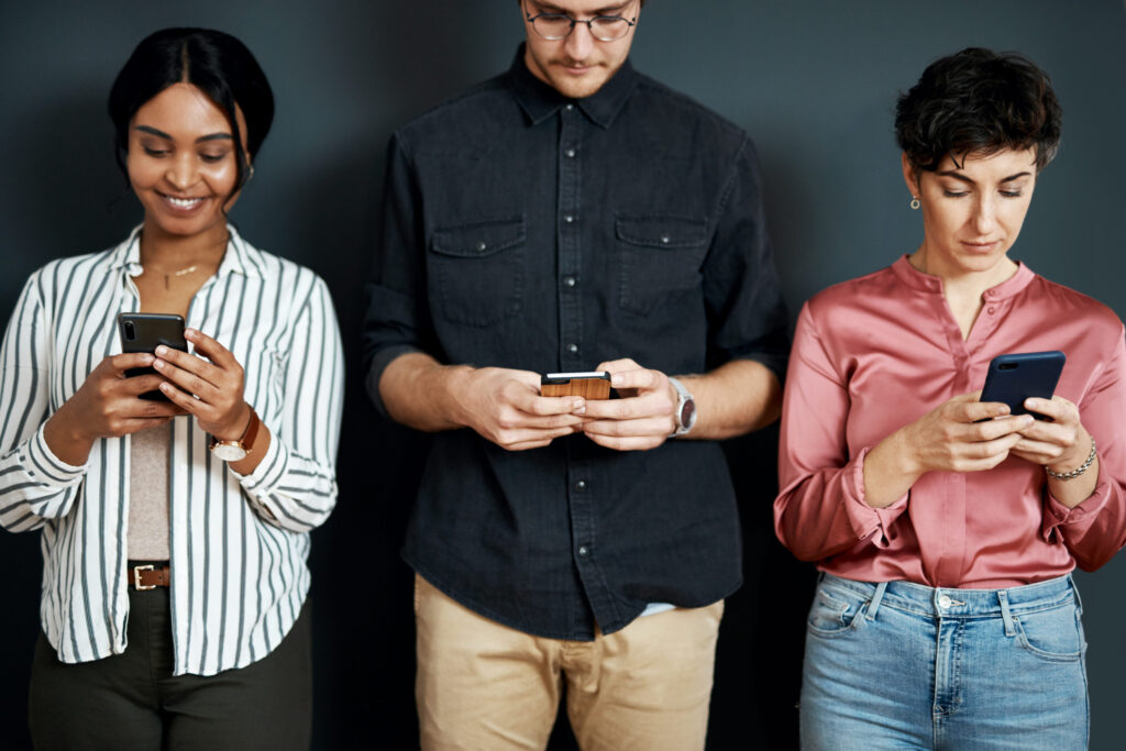 a diverse group of businesspeople standing against a gray background and texting on their cellphones