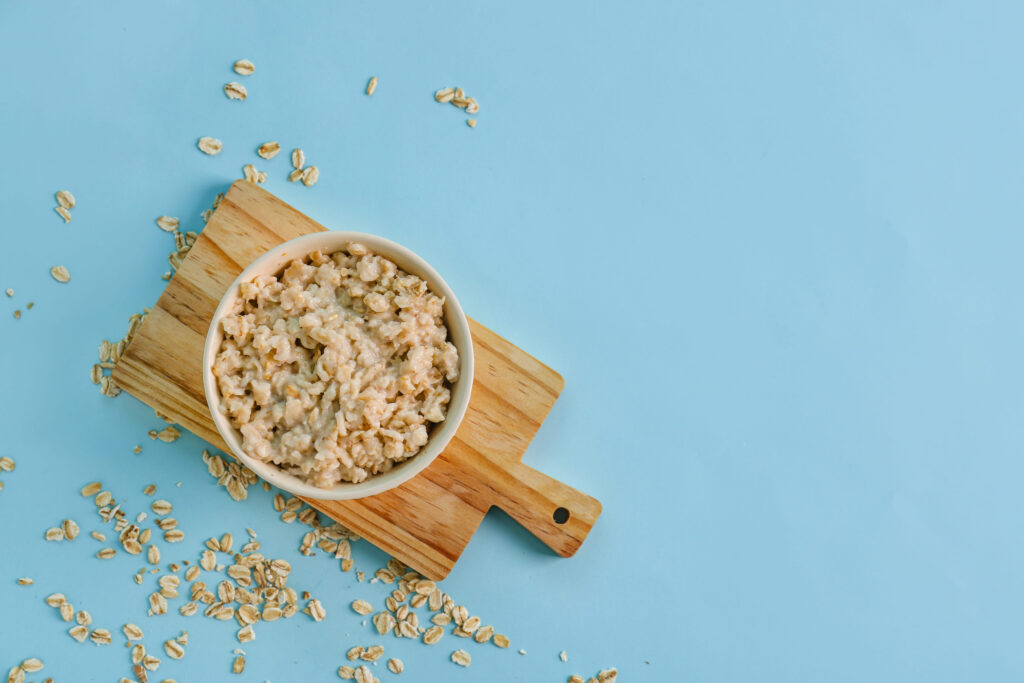 Board and bowl with tasty oatmeal on blue background