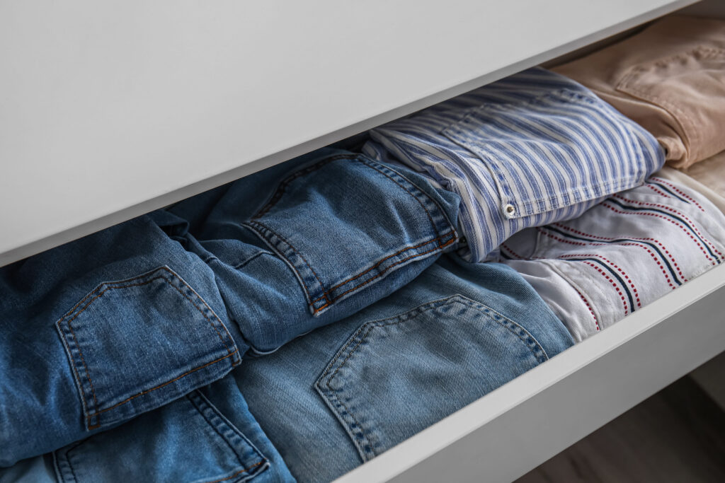 Open drawer with folded clothes in room, closeup