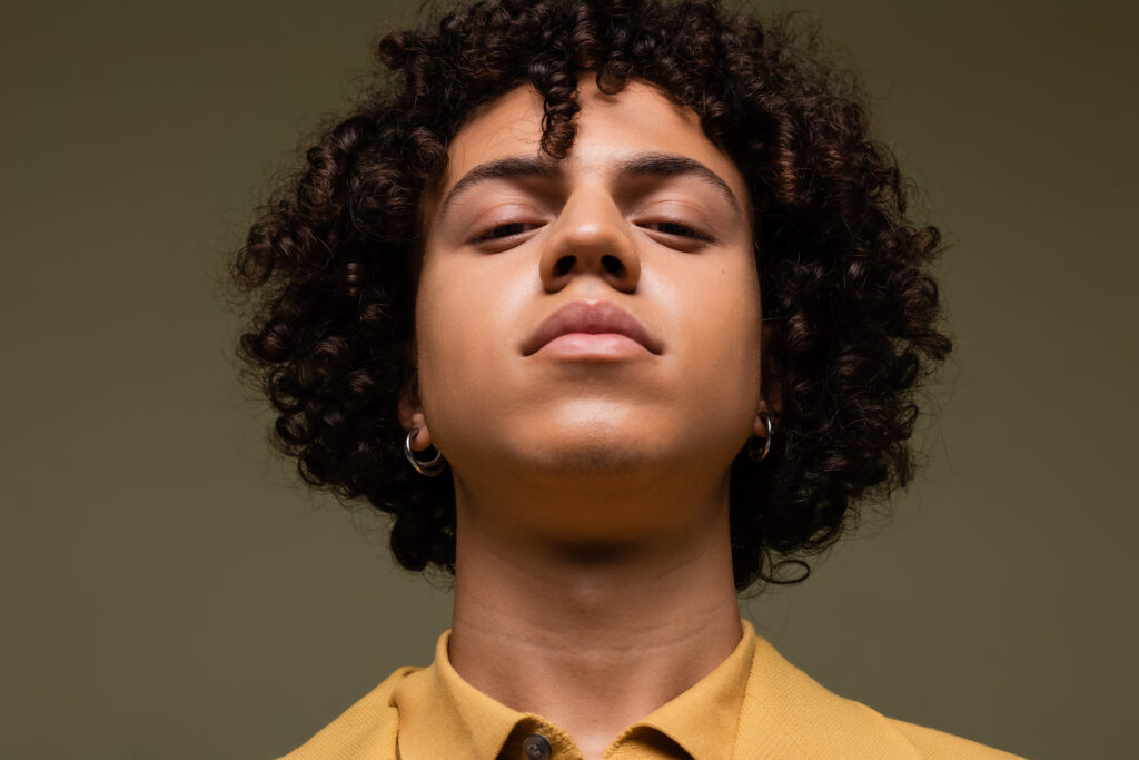 portrait of young african american man with curly hair looking at camera isolated on grey